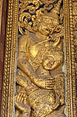 Wat Xieng Thong temple in Luang Prabang, Laos. Detail of a wooden door of the sim with gilded carvings on a red background.